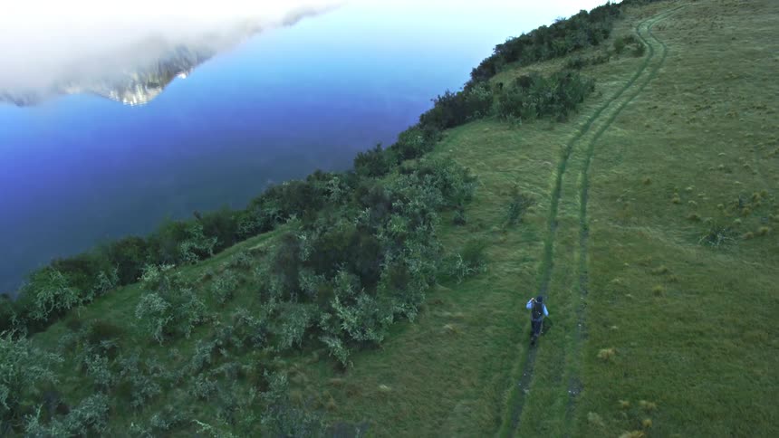 A man walks down tire tracks in a field on the lake edge
