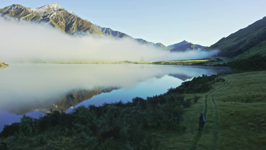 A man follows tire tracks as he walks along the edge of a lake