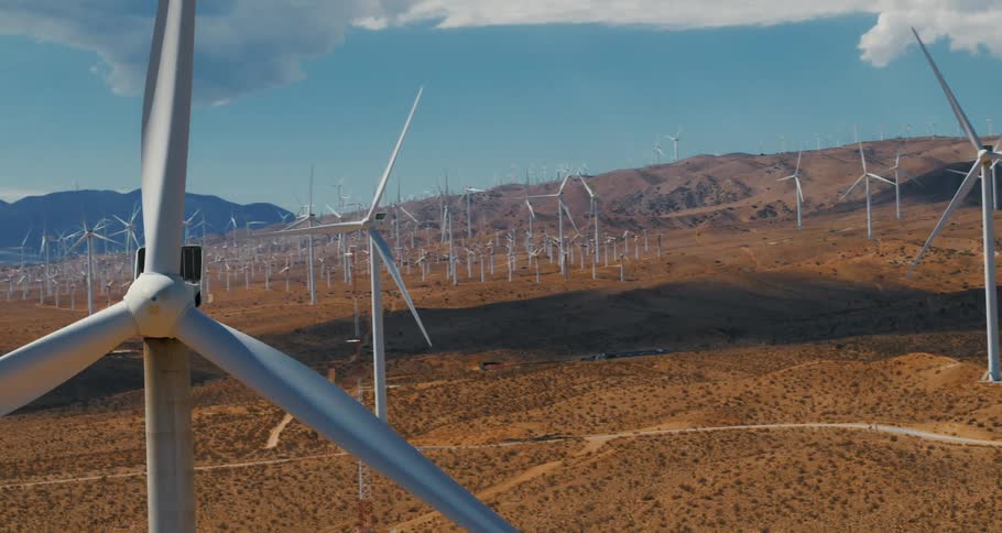 Dozens of wind turbines spin in a field near rolling hills
