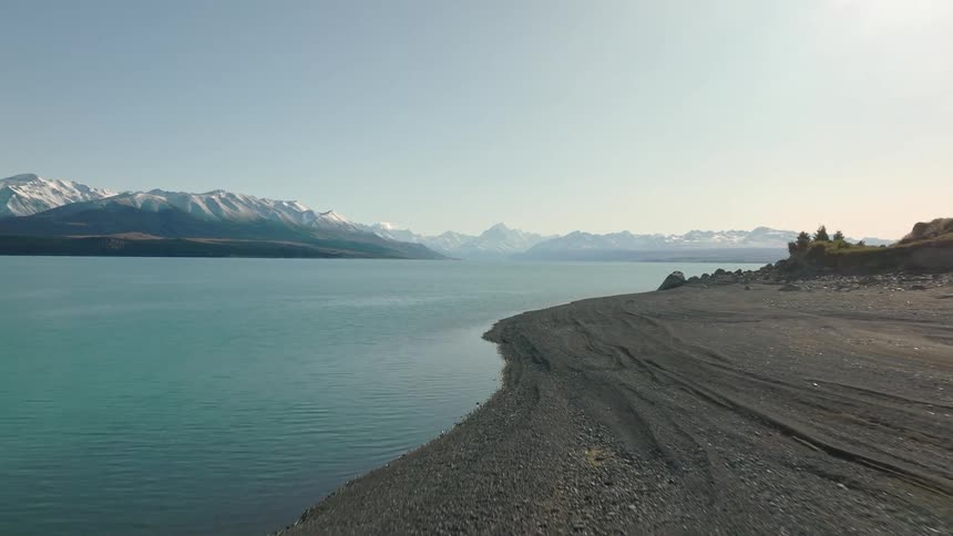 Calm sea water surrounds a beach and snow capped mountains