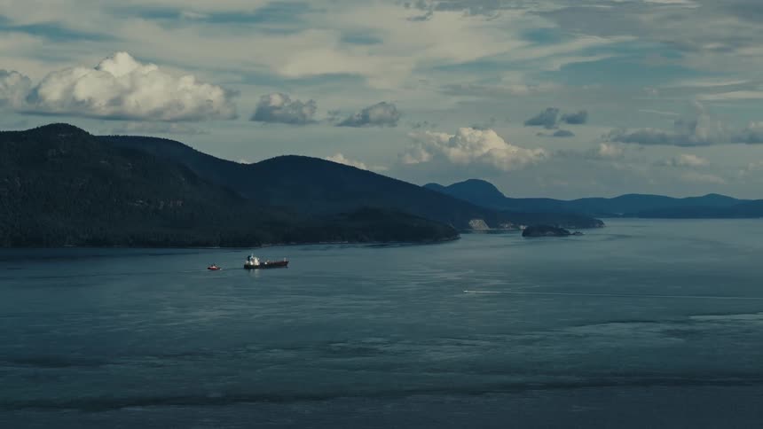 A ferry pulls a small boat through the sea past a mountain range