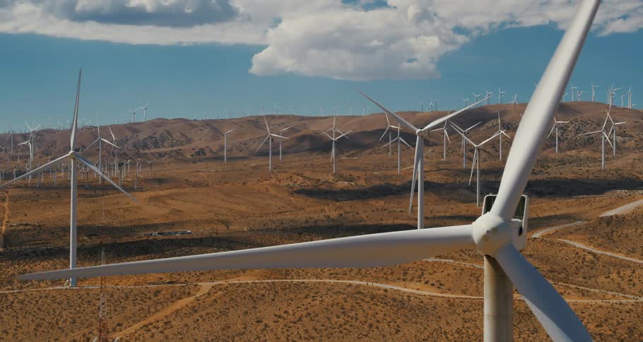 Wind turbine blades rotate on field and hill under a cloudy day