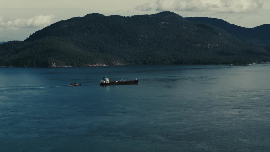 Aerial view of cargo ship and boat sailing near mountainous area