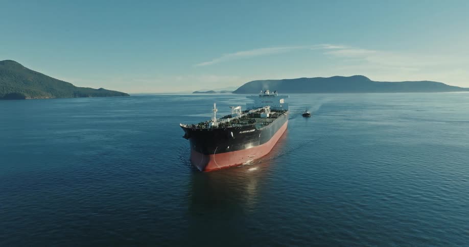 Freighter and boat move across water with mist covered forested mountains in the background
