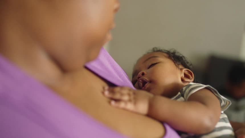 Mom holds baby close to her chest looking down with love as he sleeps