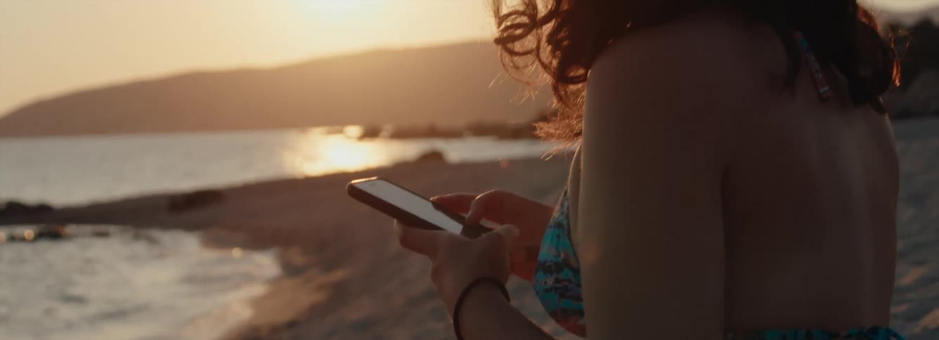 A woman stands on the beach and uses her cell phone