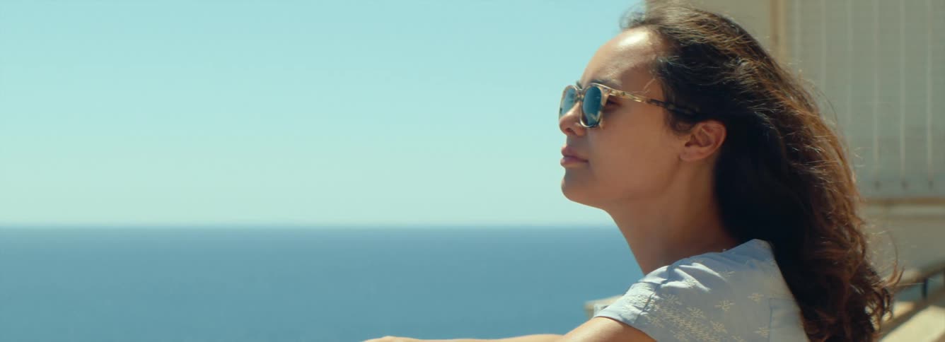 A woman is relaxing outdoors and looking at the ocean