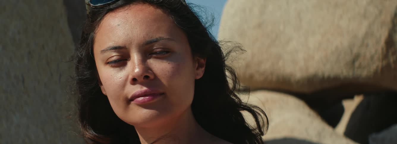 A portrait of a woman in front of large rocks outside turns her head