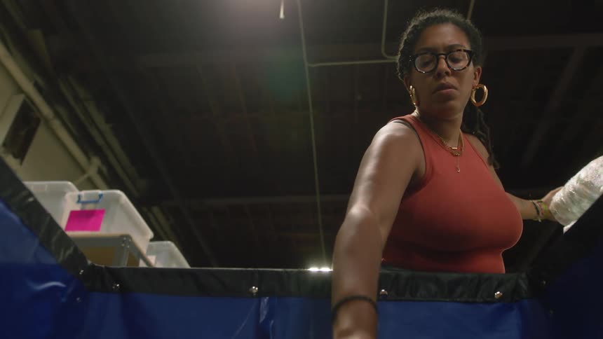 Woman selects items and places them in large blue vinyl walled cart in warehouse