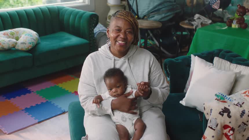 A woman sits at home and holds her baby