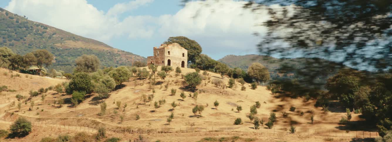 A dilapidated home sits atop a hill below a mountain in the Mediterranean