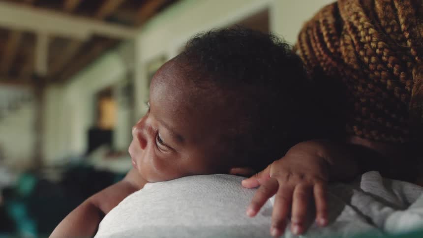 Woman stands holding baby against her shoulder in large room