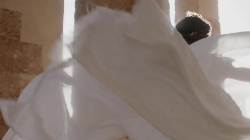 Wind blows through a woman's toga as she stands near pillars