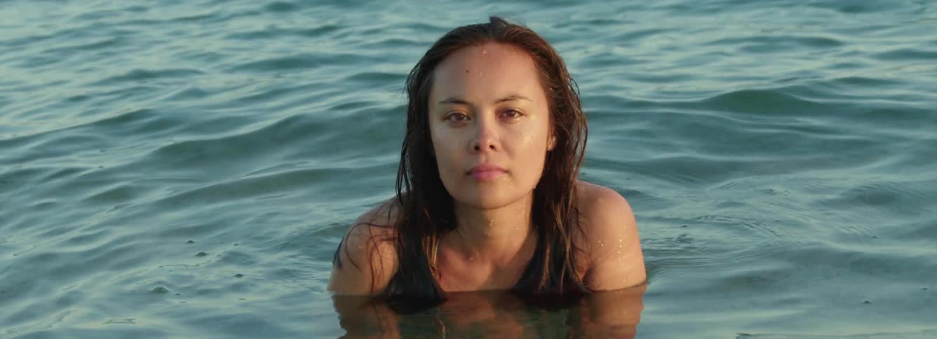 Young woman sitting on a beach submerged up to her shoulders looking at the camera