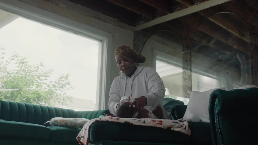 A woman at home puts a shirt on her baby