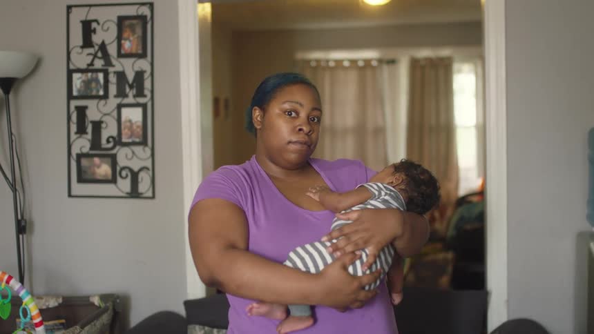 A woman at home holds her baby and gently rocks him