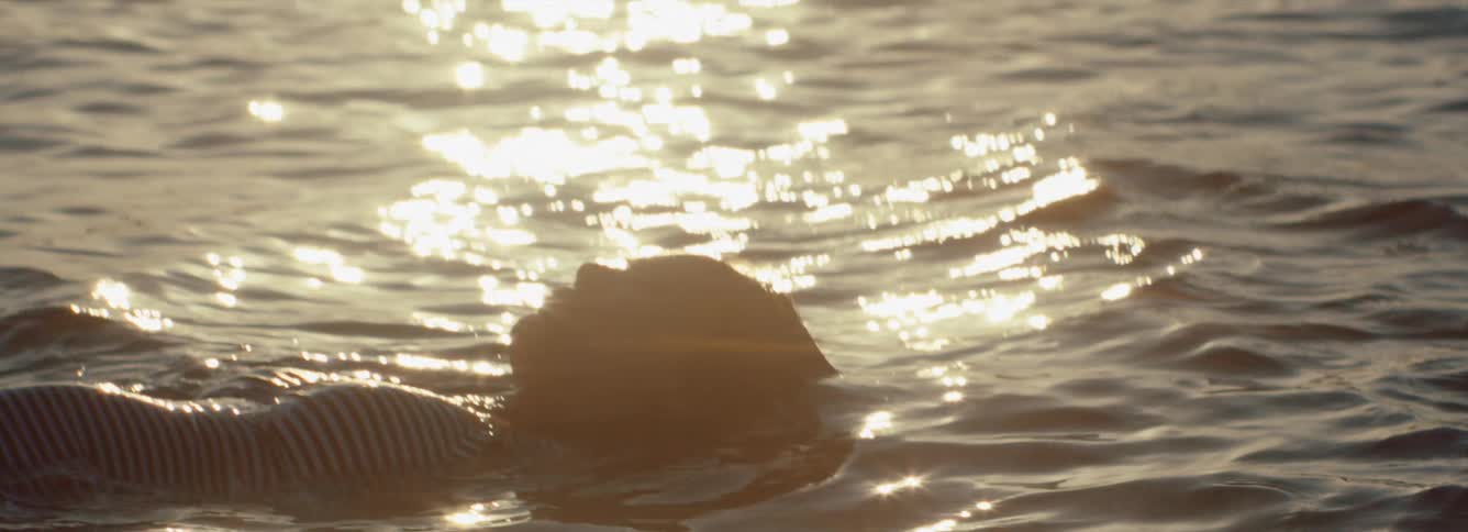 A person is laying in the ocean water during dusk, anamorphic flare