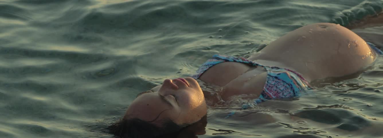Young pregnant woman wearing a swimsuit floating on the ocean at sunset