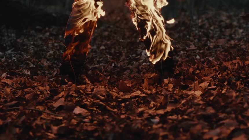 Man with black pants burns in fire in the forest standing on dead leaves