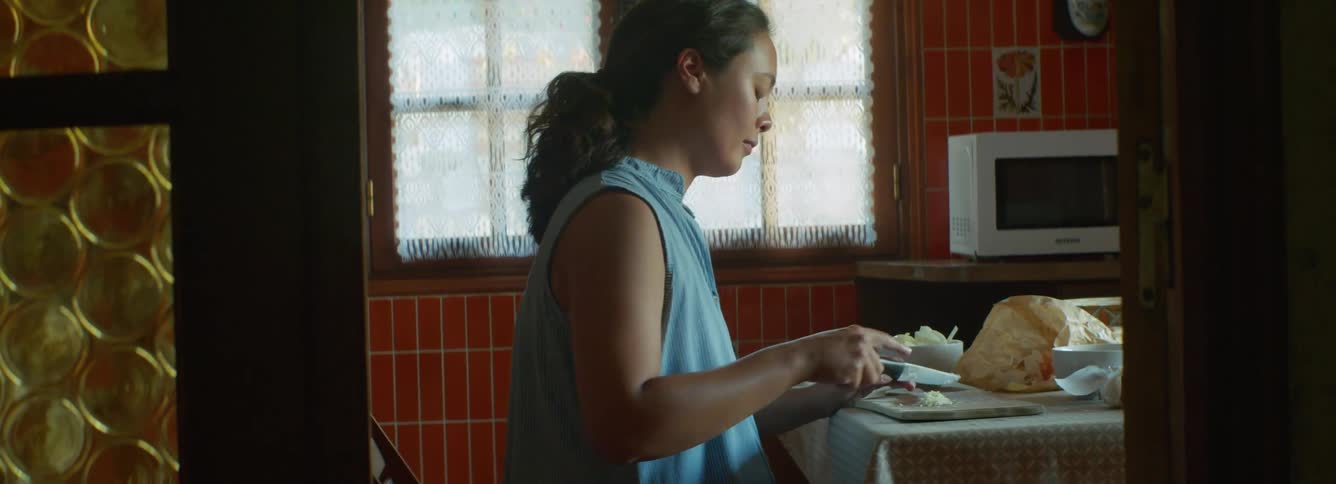 A pregnant woman chops onions on a chopping board in a home kitchen during the day