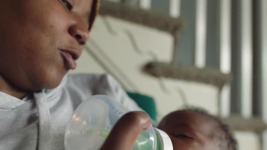 Mother with gray hoodie feeds baby with bottle