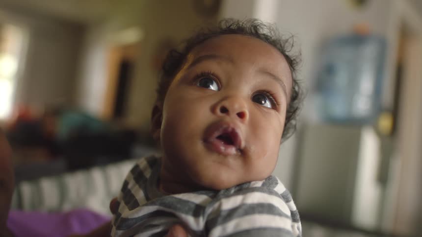 A baby being held by their mother is looking around in wonder with a smile