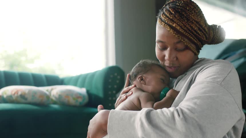 A woman lifts and kisses a baby before cradling the baby against her chest