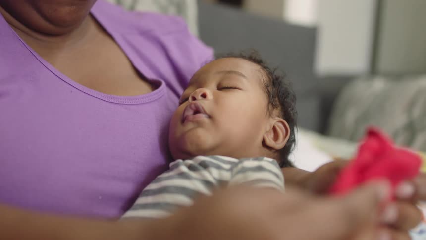 A woman holds her sleeping baby while folding laundry