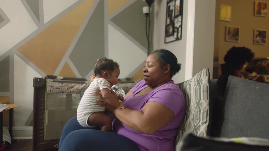 A woman hoists her grandchild in the air while sitting on the couch