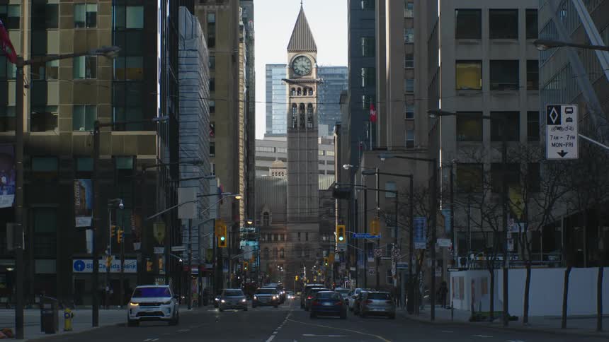A city street with cars a pedestrian and high rise office buildings and a clock tower