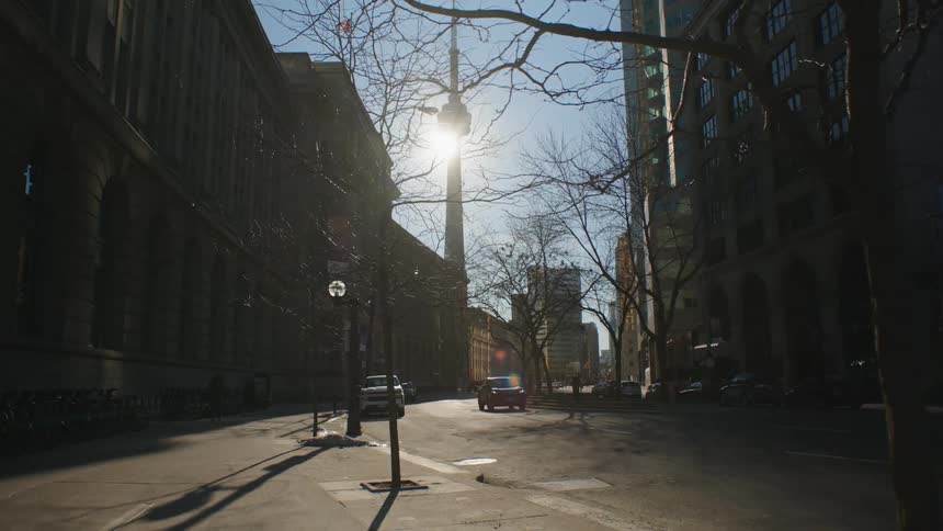 A car traveling on a city street with the silhouette of the cn tower in the skyline