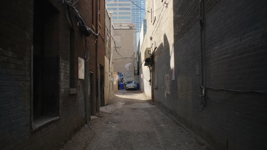 A car is parked in an alley and tall downtown buildings are in the distance