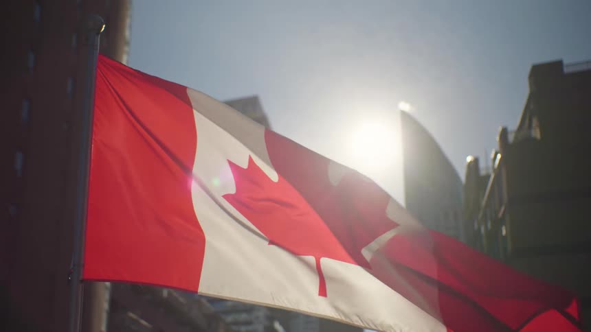 Sun shines between downtown skyscrapers and through canadian flag blowing in the wind