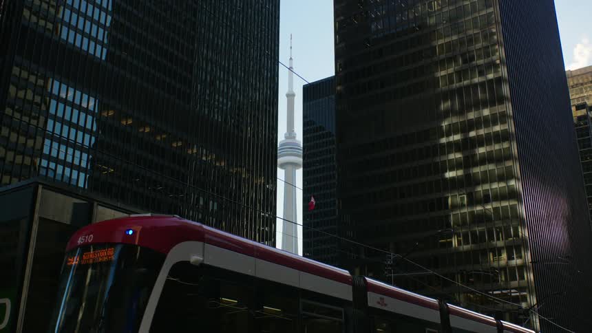 Red topped light rail train moves past skyscrapers with space needle visible in the distance