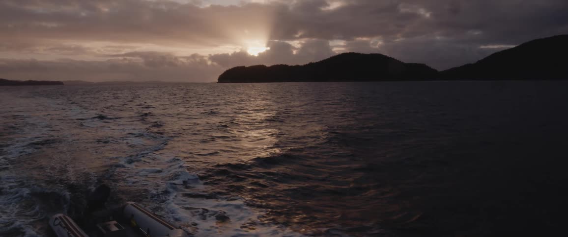 Inflatable boat being towed on the ocean next to the silhouette of mountains at sunset