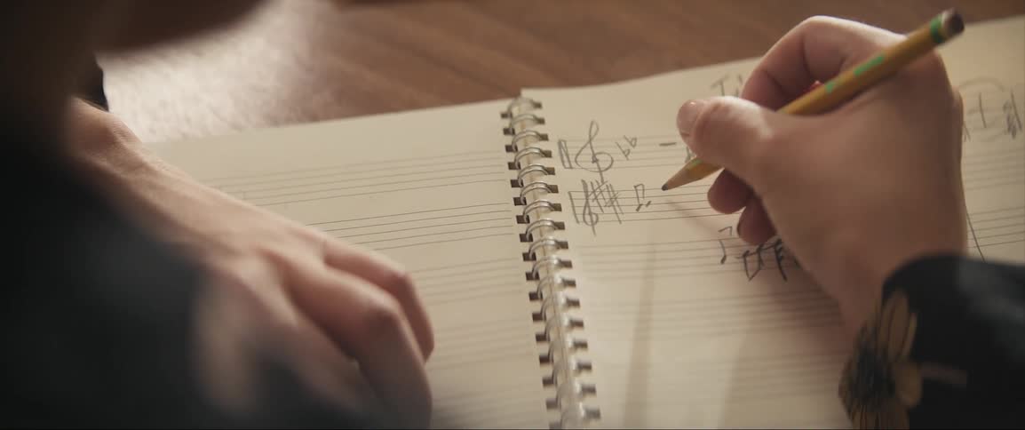 A person is writing music notes in a notebook