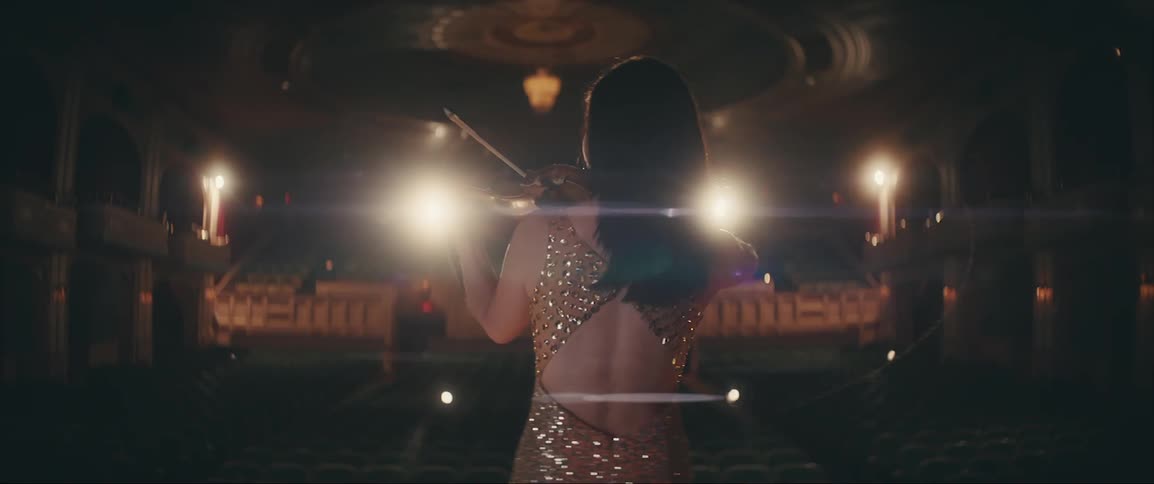 Violinist practices instrument while standing on stage in empty theater