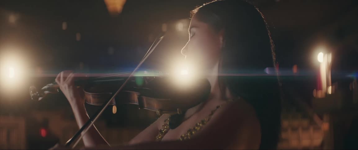 A female violinist raises her violin and begins to play while standing on a stage in a theater