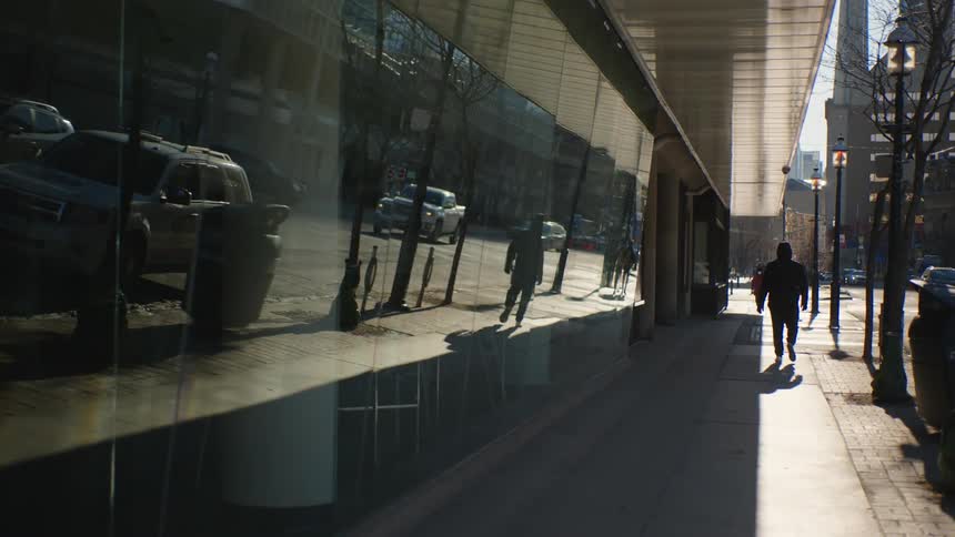 Reflective glass reflects traffic and pedestrian walking along sidewalk toward the intersection
