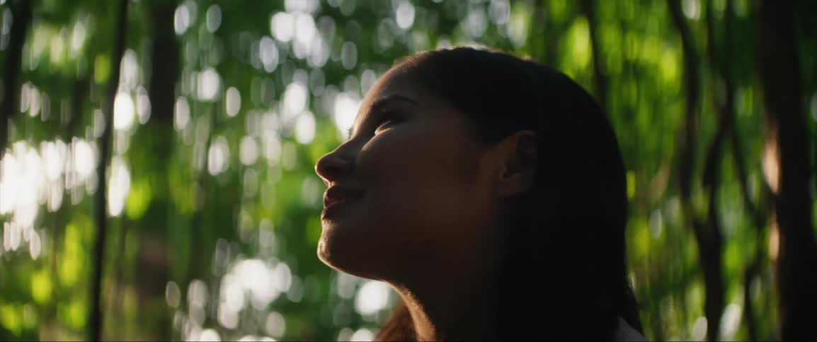 A woman smiling with her face uplifted to the trees and sunshine
