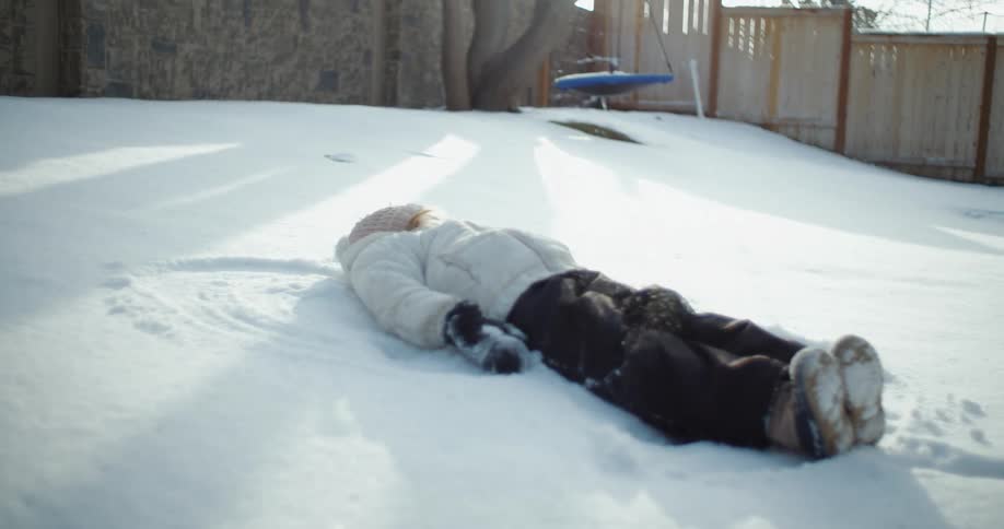 A young child making a snow angel in their backyard on a winter day