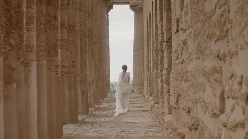 Woman in white dress walks between pillars and wall