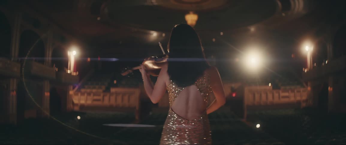 Lights shine on a woman on stage wearing a sequin dress and playing a violin