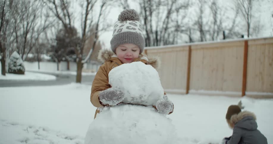 A child carries a giant snowball to build a snowman