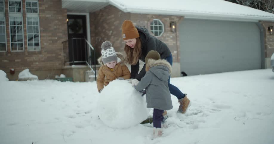 Mother and daughters build a snowman together
