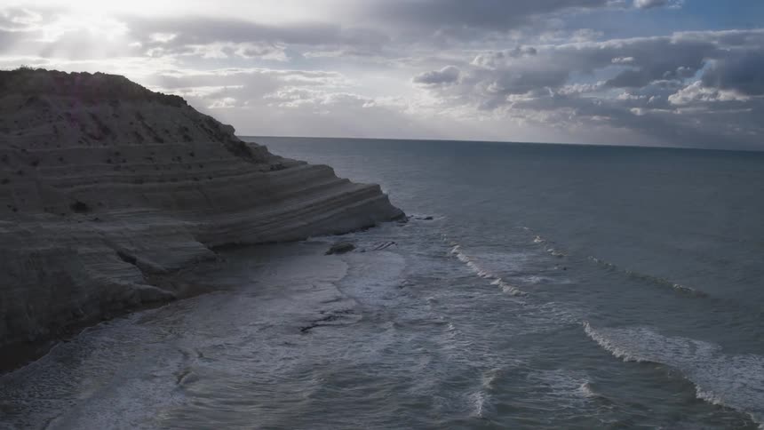Waves roll onto a sandy, hilly shore