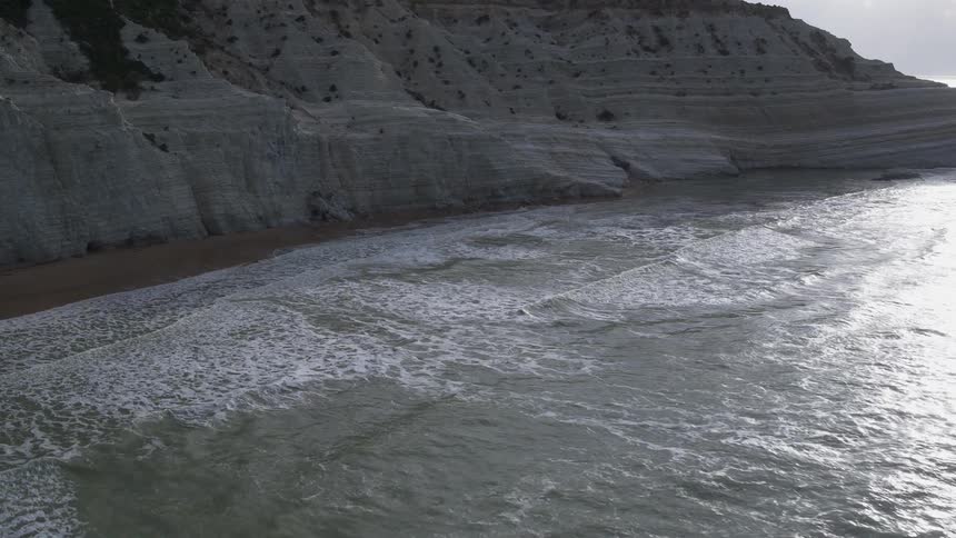 Waves break against white cliffs during the day