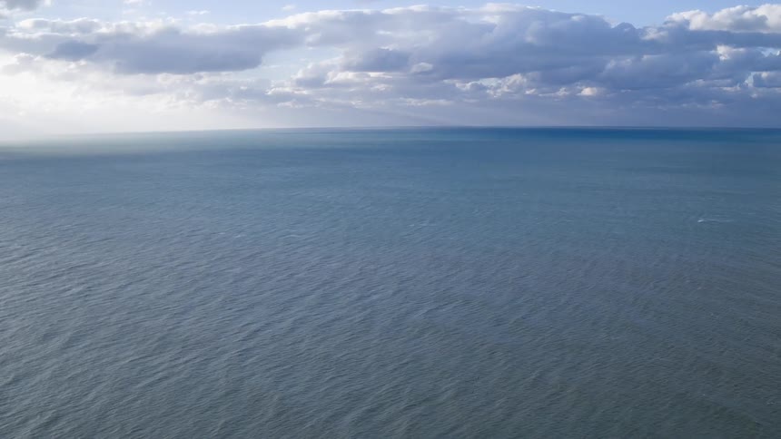 The ocean and horizon are seen under a cloudy day sky