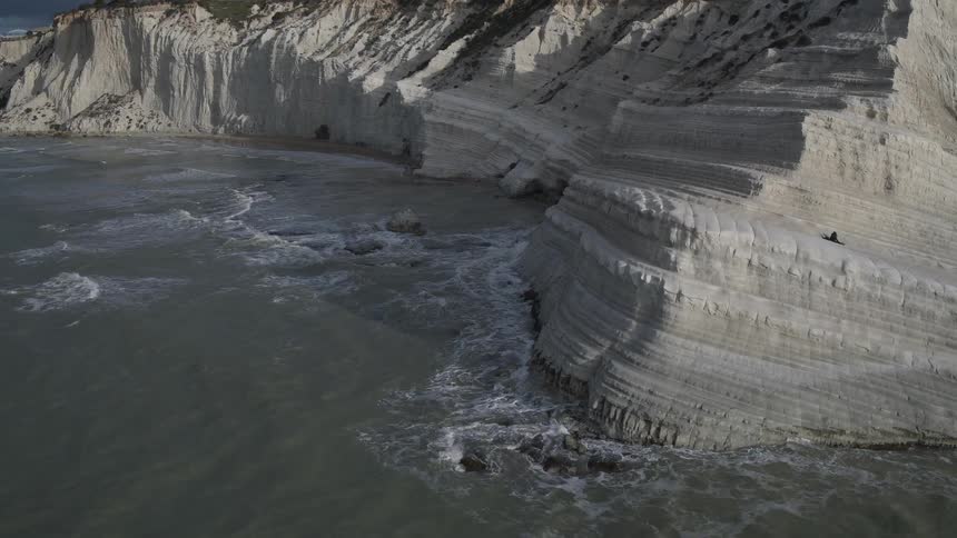 Waves hit the base of a layered rock formation