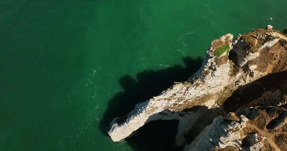 A sheer cliff looms over the ocean during the day